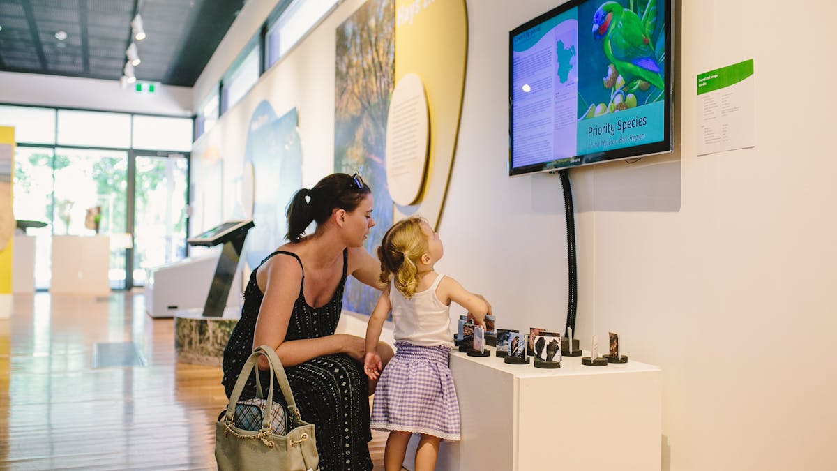 A girl and lady interactive with a exhibition item on bird species