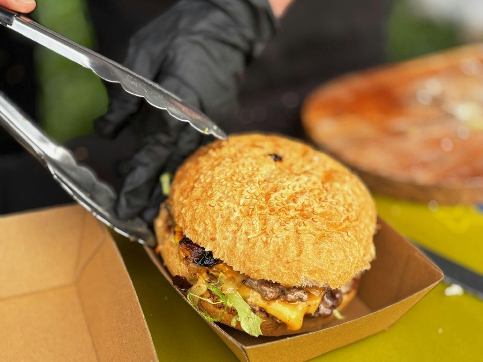 A burger being placed with tongs in to a take away box