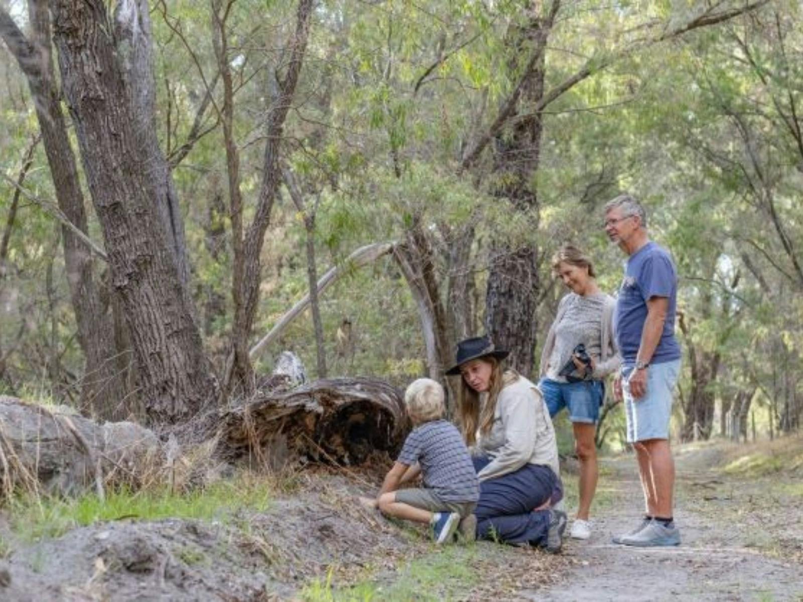In nature2  adults standing and one young boy kneeling next to a Female tourguide wearing  black hat