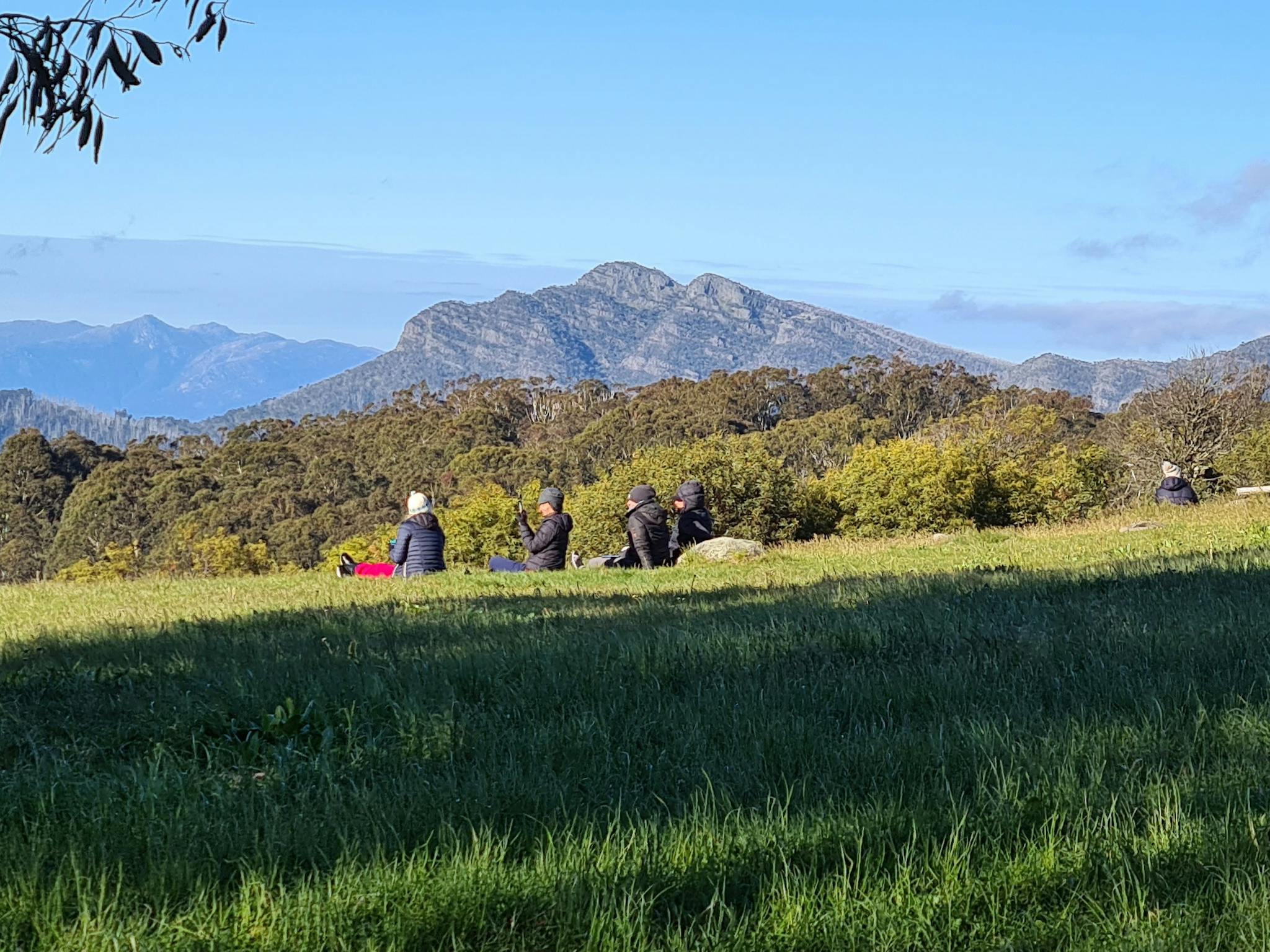 A group of hikers soaking up the sun at Clear Hills with a view of Mt Cobbler and Mt Buffalo.