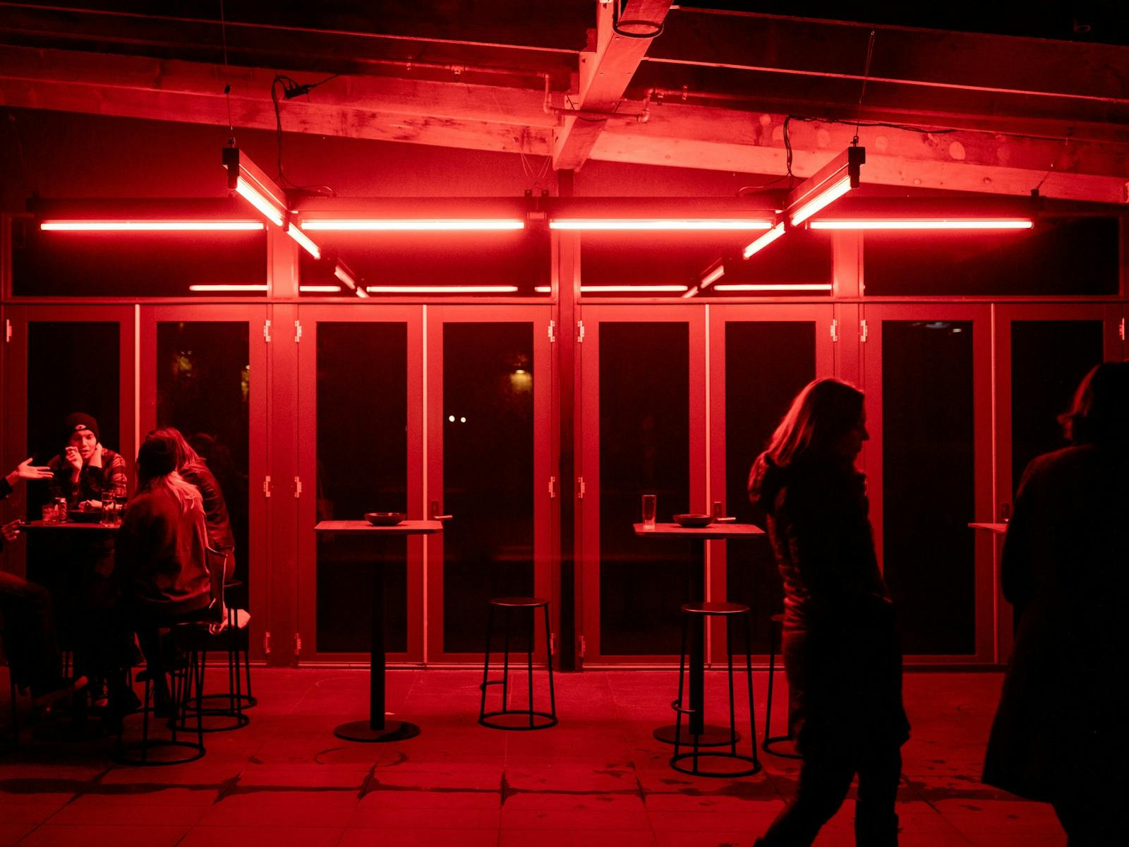 Red neon lights illuminate the upstairs courtyard, with people seating and two tall bar tables