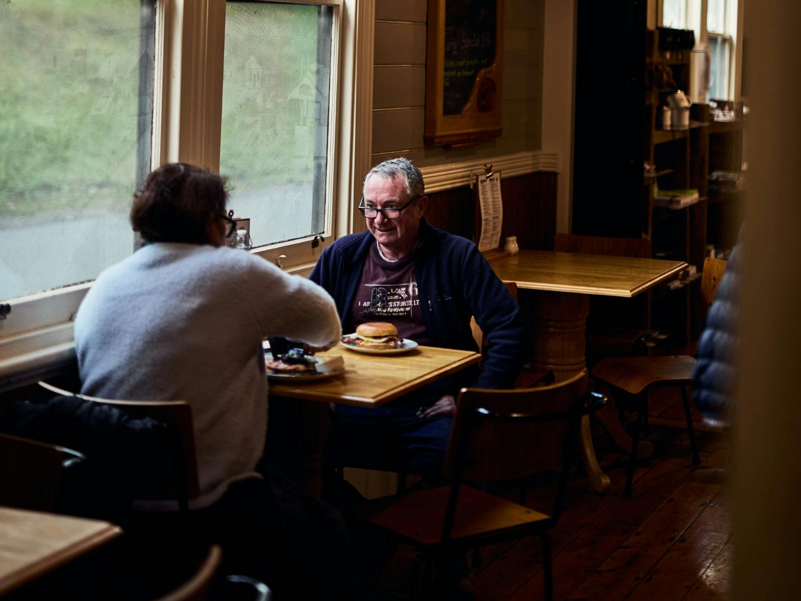 Couple sits at a table by a window with a burger on the table