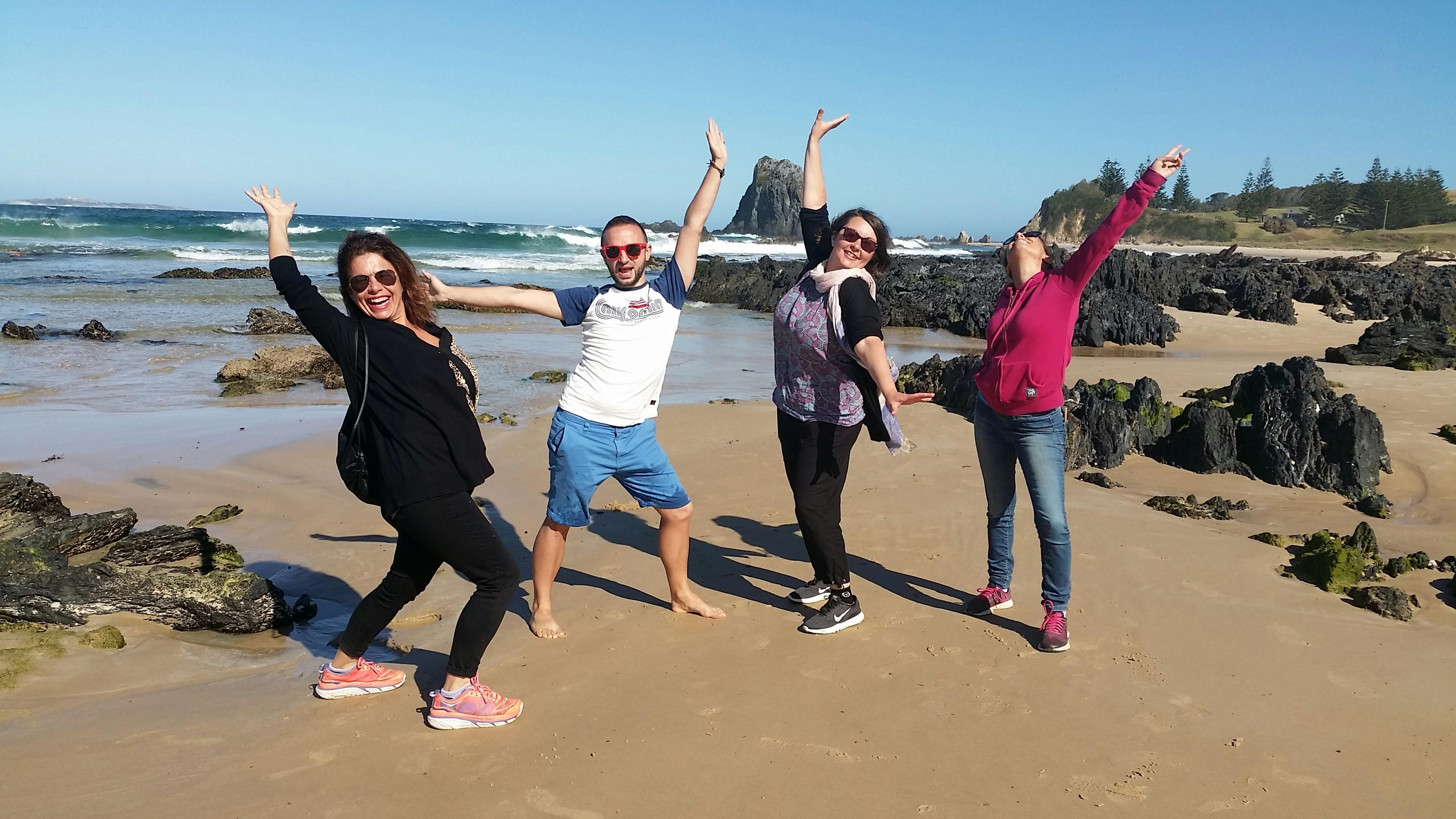four people with arms in the air on the beach in front of rock formations