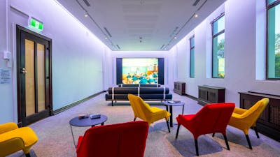 A light filled space with yellow and red chairs and a large screen playing documentaries