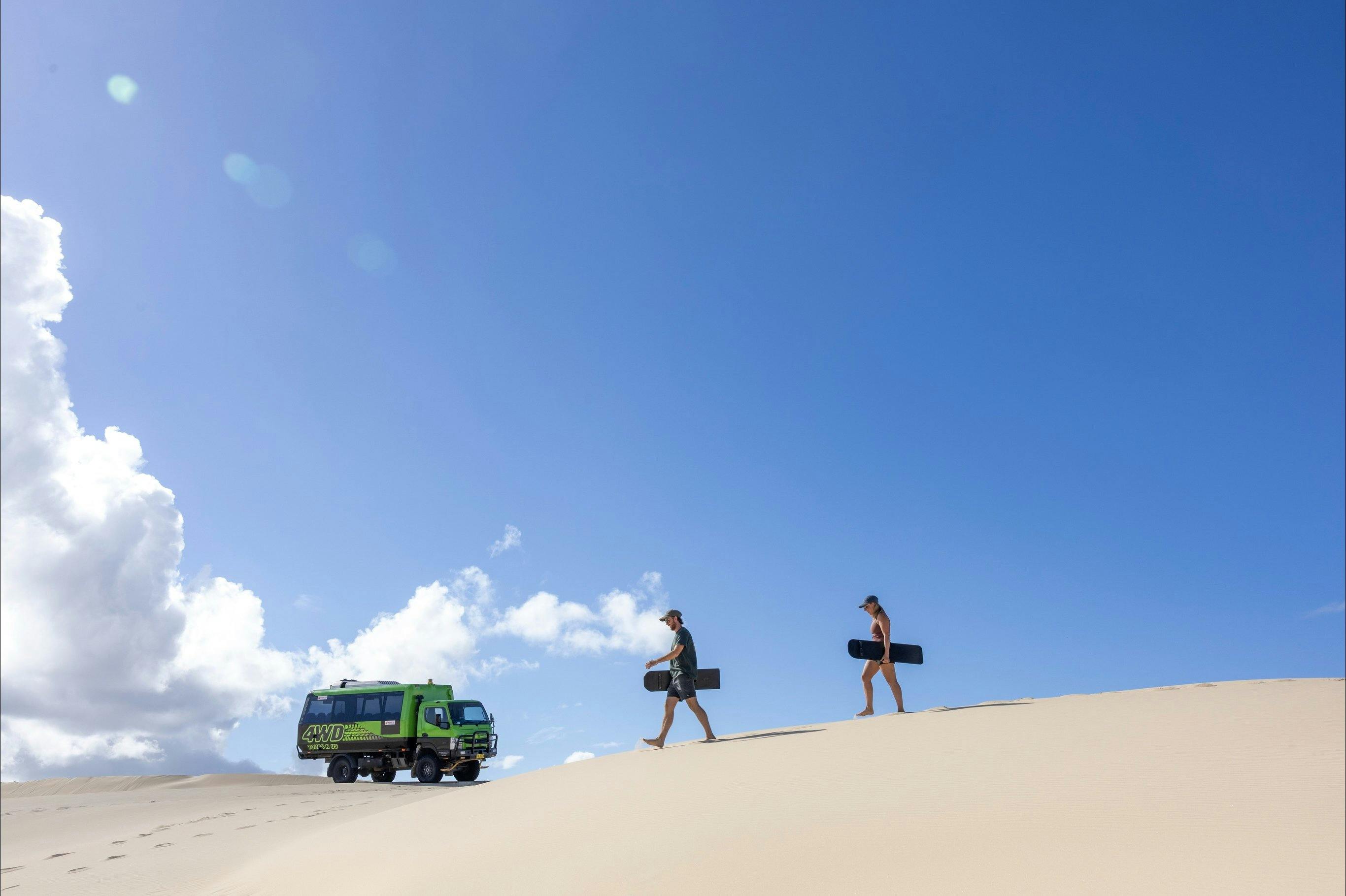 A group of young people walking side-by-side holding sandboards as they head toward a large sand dun