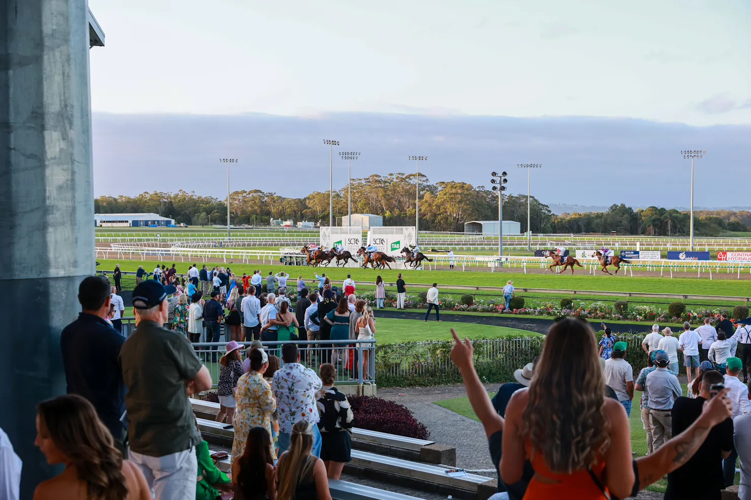 Crowd watching and cheering on the horses race on the track past the finish line.