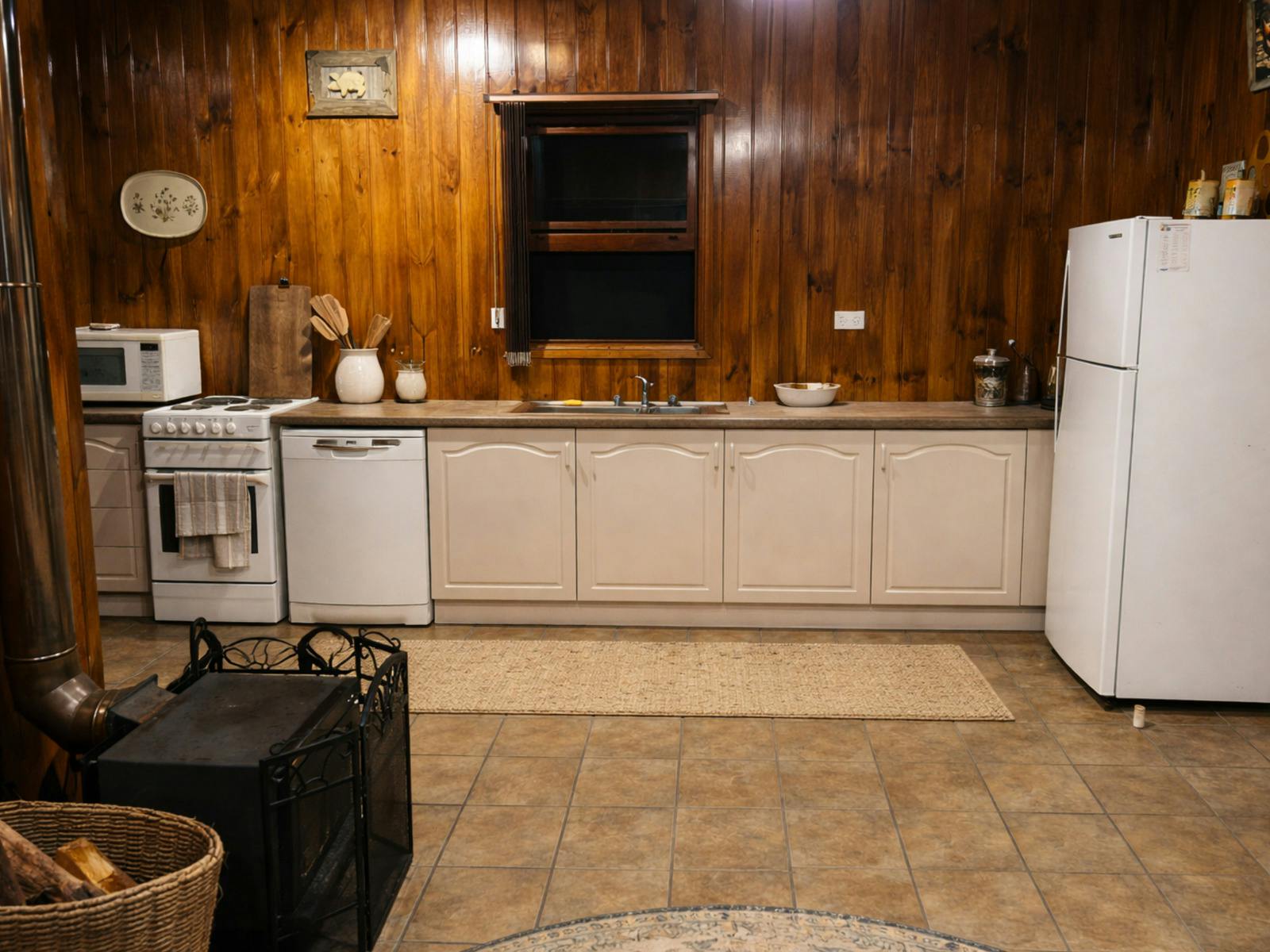 A rustic timber-lined kitchen with a stove, microwave, sink, fridge and slow combustion wood heater