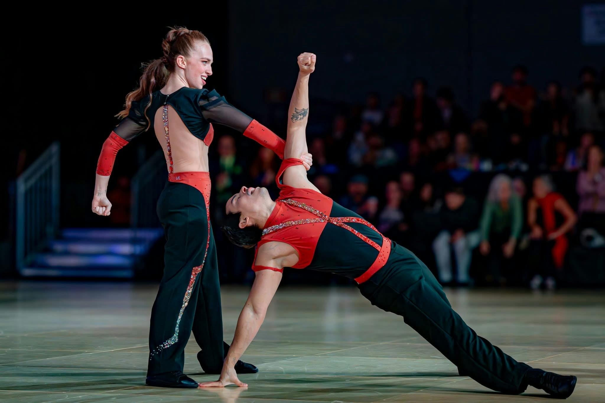 West Coast Swing dancers in a striking pose at a competition with cheering audience behind them.