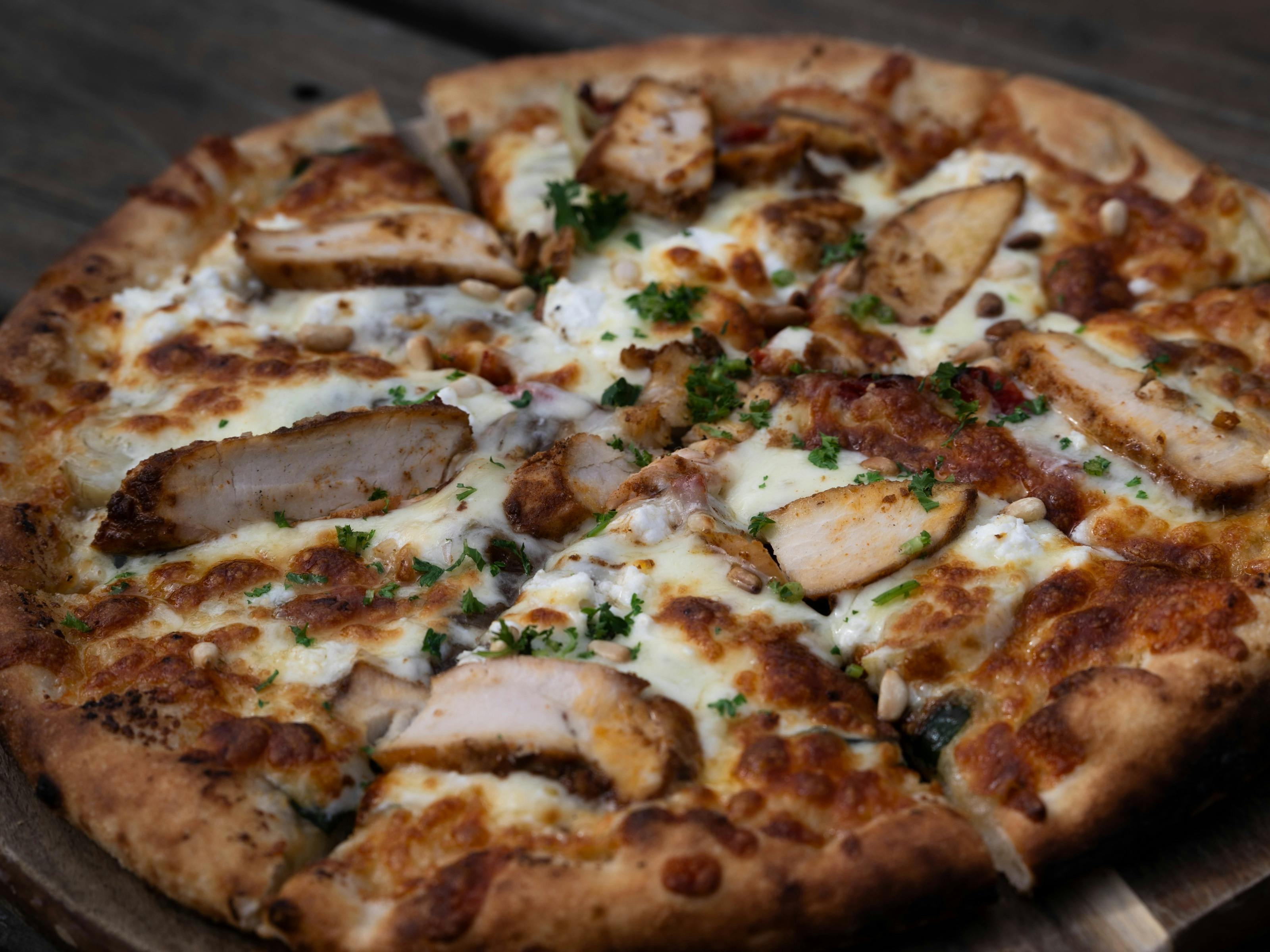 Woodfired Mother Clucker pizza with chicken, spinach, feta, artichokes, mozzarella and pine nuts.