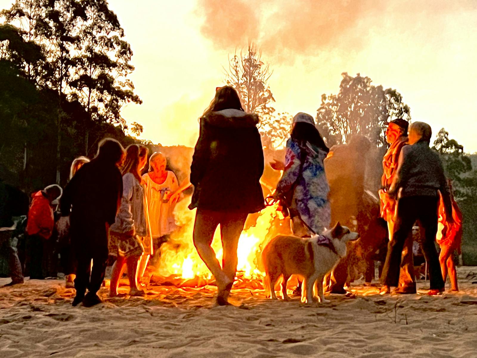 Figures gather around a fire at twilight