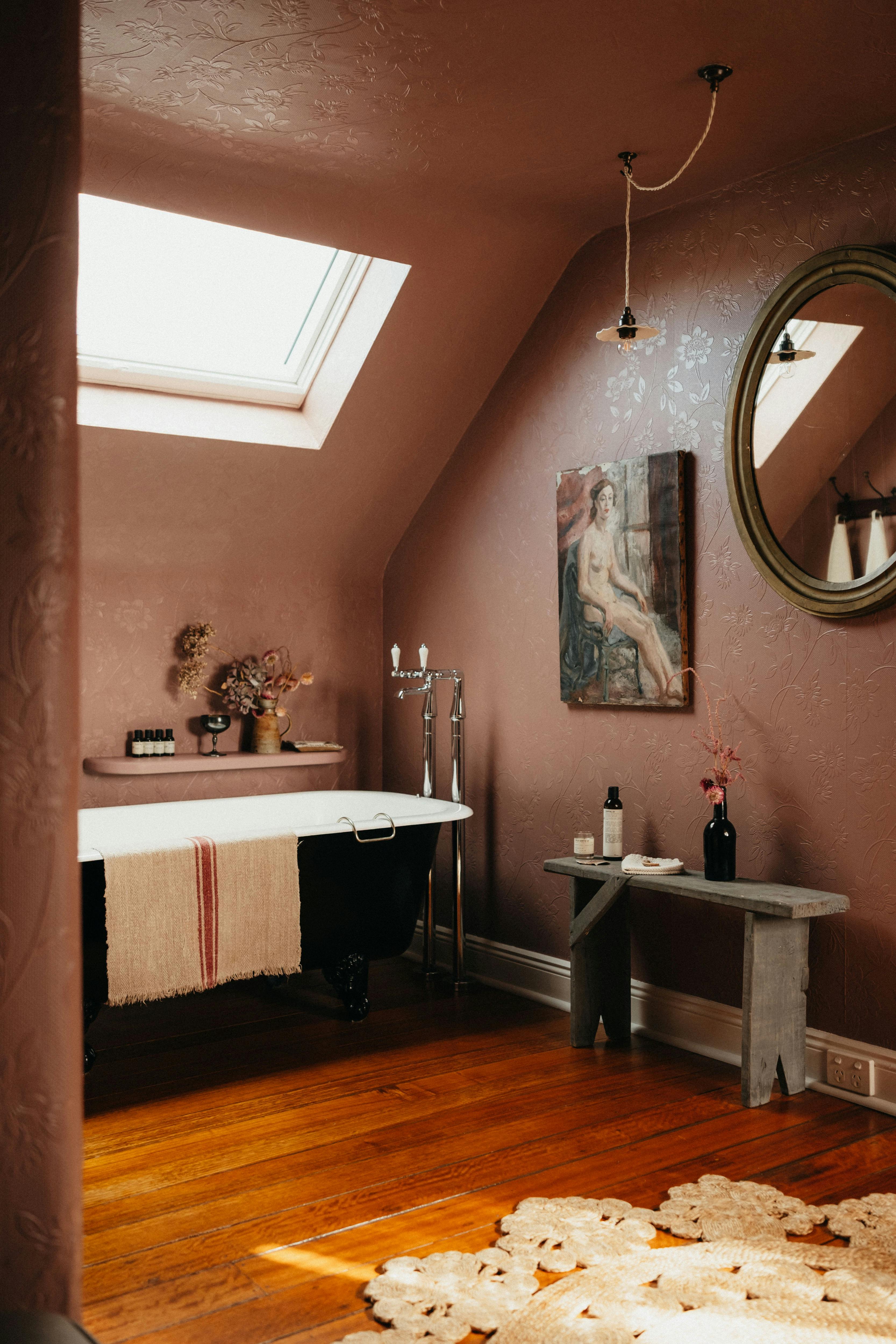 Attic bathroom with clawfoot bath, skylight, pink walls and vintage details.