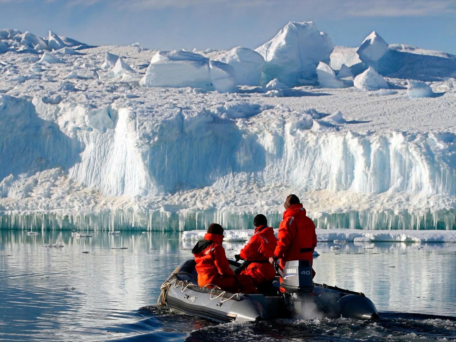 Three people in a small inflatable boat looking at the large ice formation in front of them.