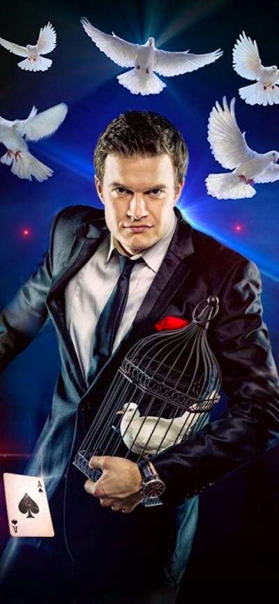 a magician with white doves flying above him with Playing cards falling around him.