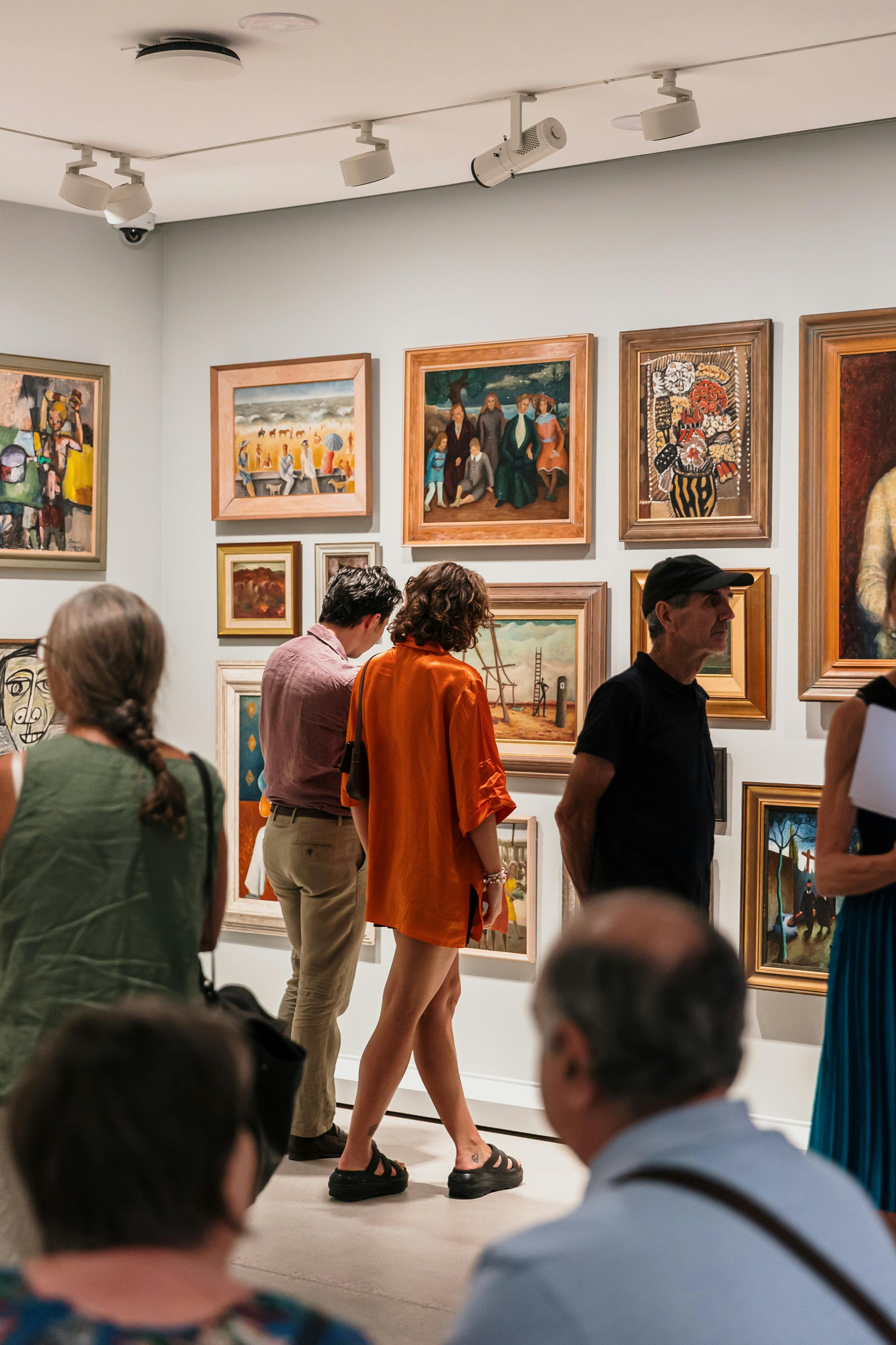 Image of two people standing in front of a wall of framed paintings in the Gallery