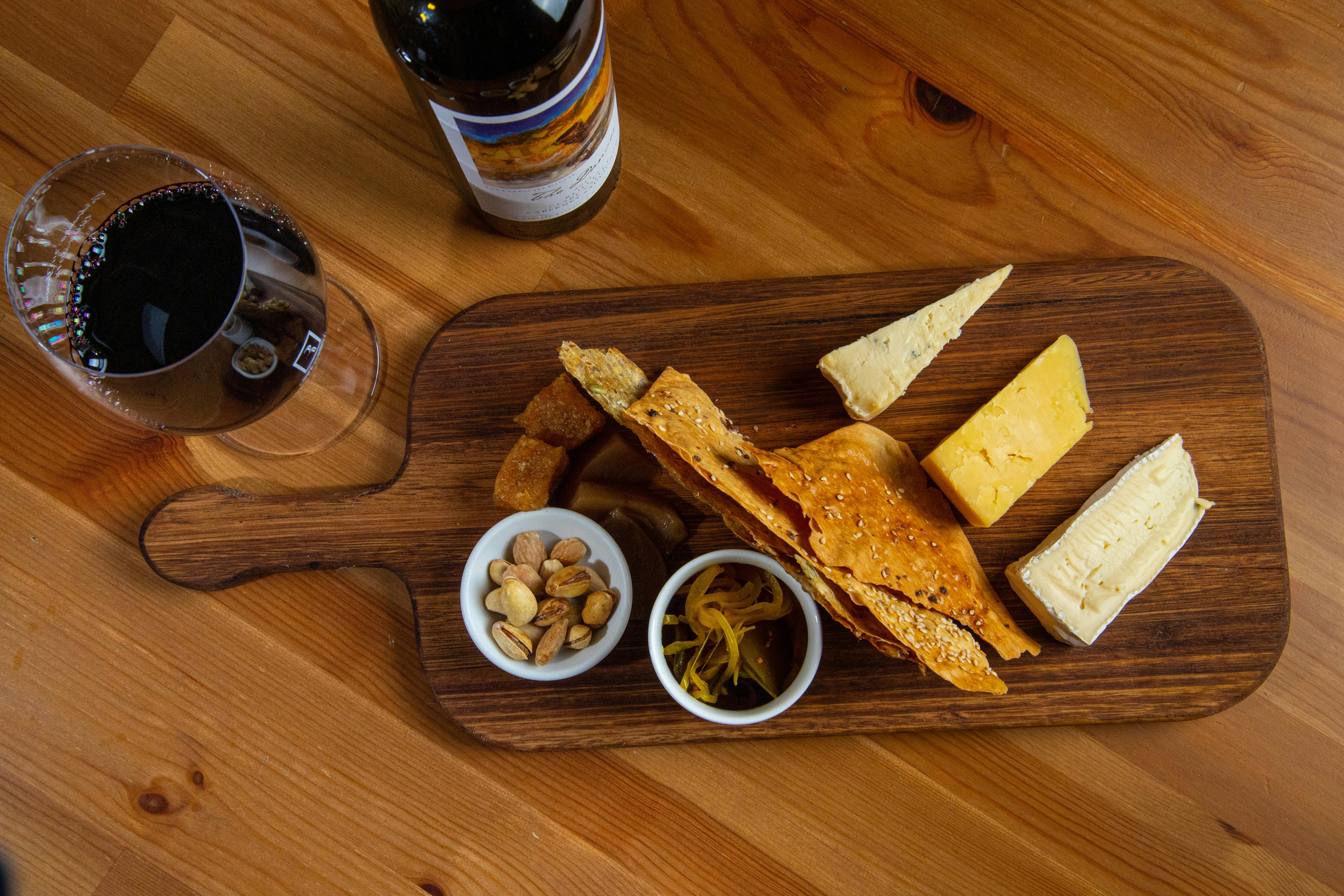 Cheese board with 3 cheeses, handmade crackers and condiments next to a glass and bottle of wine