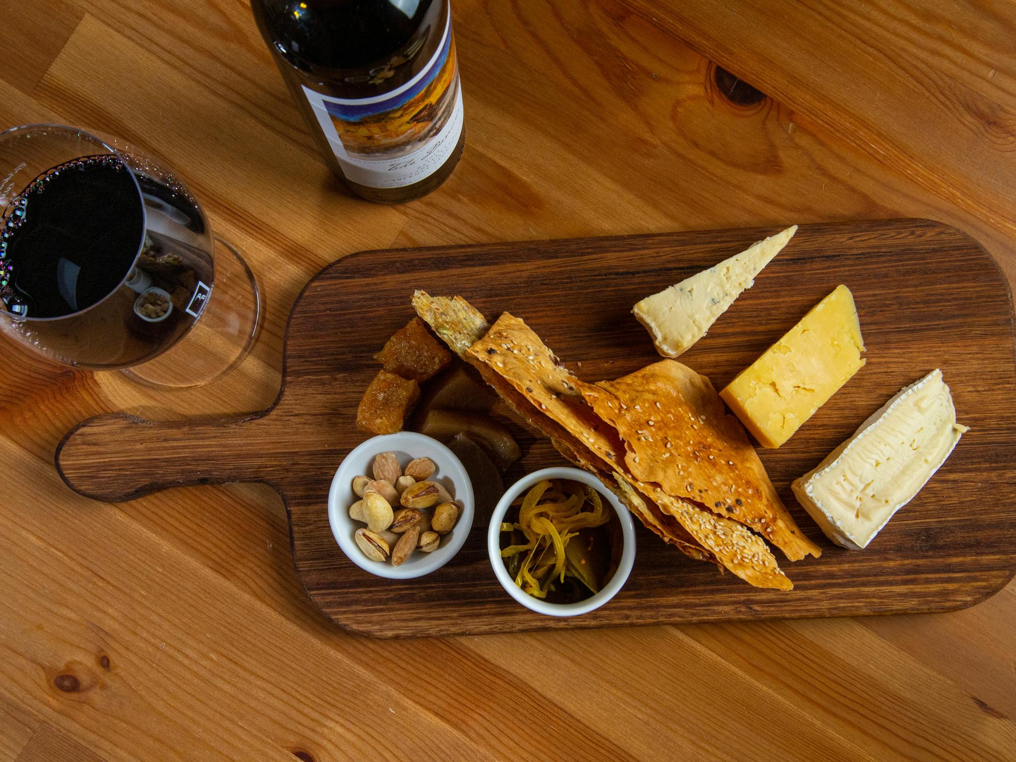 Cheese board with 3 cheeses, handmade crackers and condiments next to a glass and bottle of wine