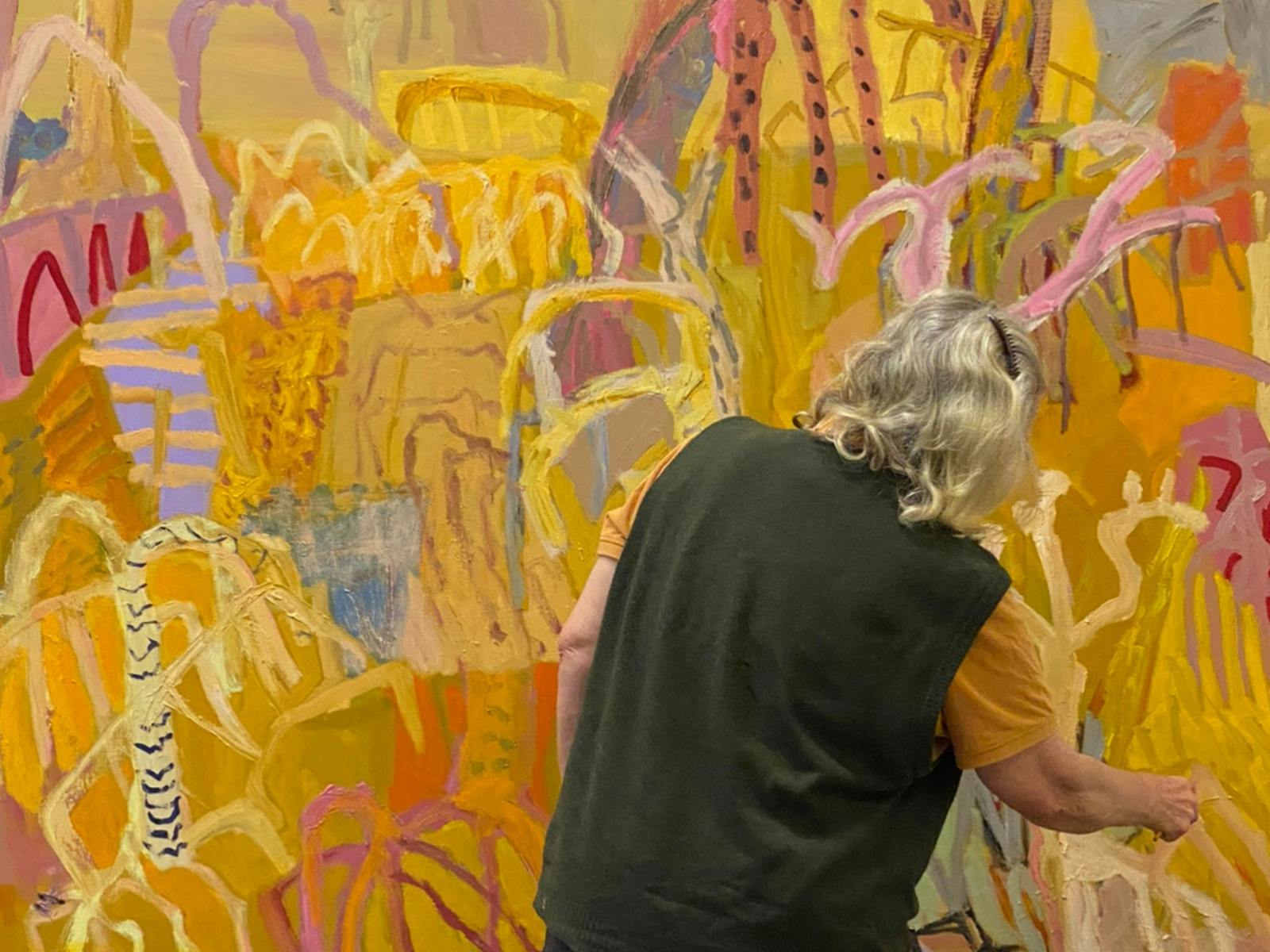 Artist Sally Stokes facing a bright, colourful abstract artwork