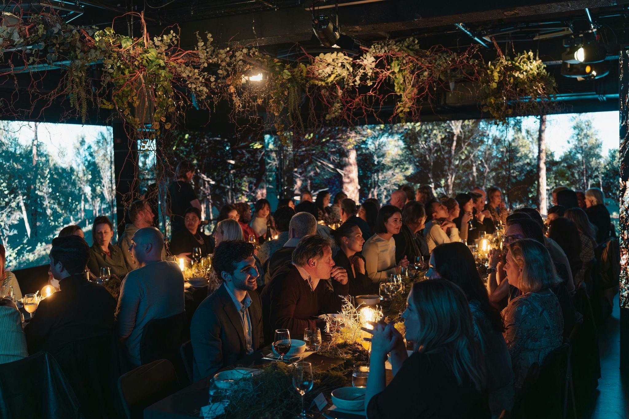 A communal dining table with forest styling and forest displayed on LED screens