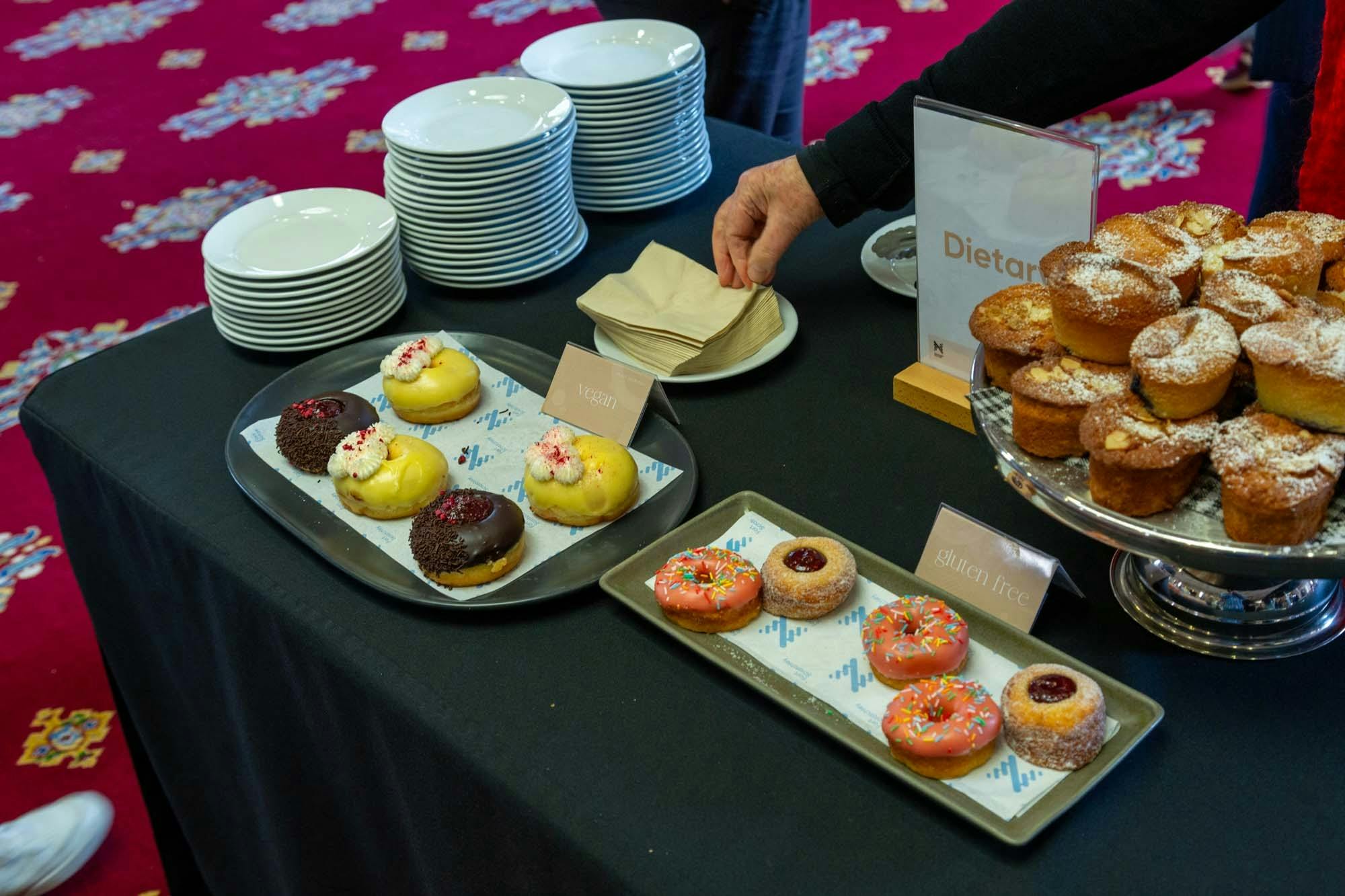 Table with black tablecloth and plates, doughnuts and cakes on it.