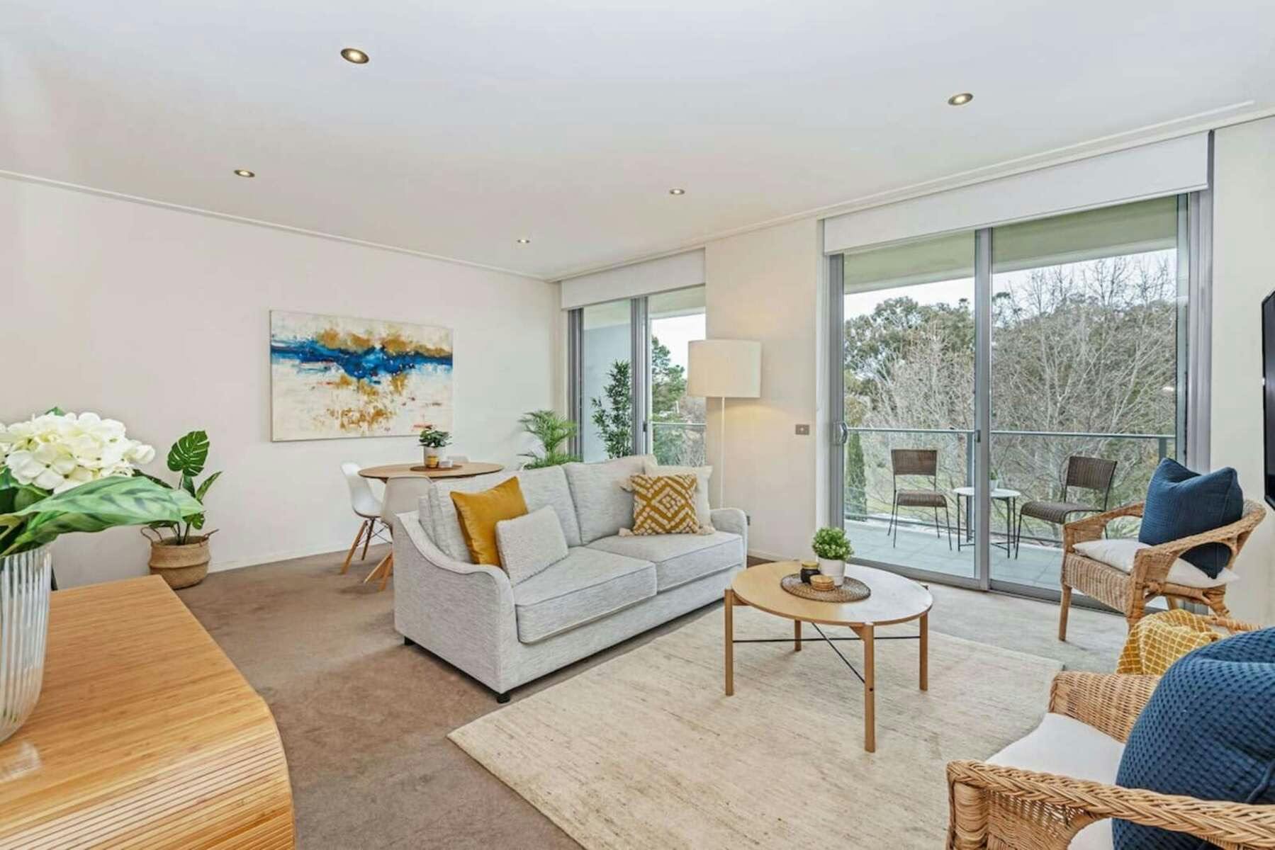 Bright living room with light grey sofa, wooden coffee table, and glass balcony doors.