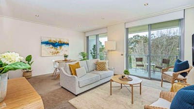 Bright living room with light grey sofa, wooden coffee table, and glass balcony doors.