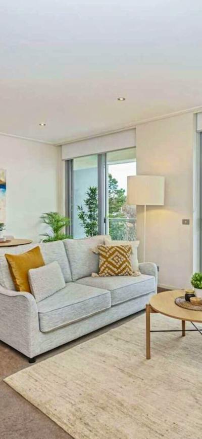 Bright living room with light grey sofa, wooden coffee table, and glass balcony doors.