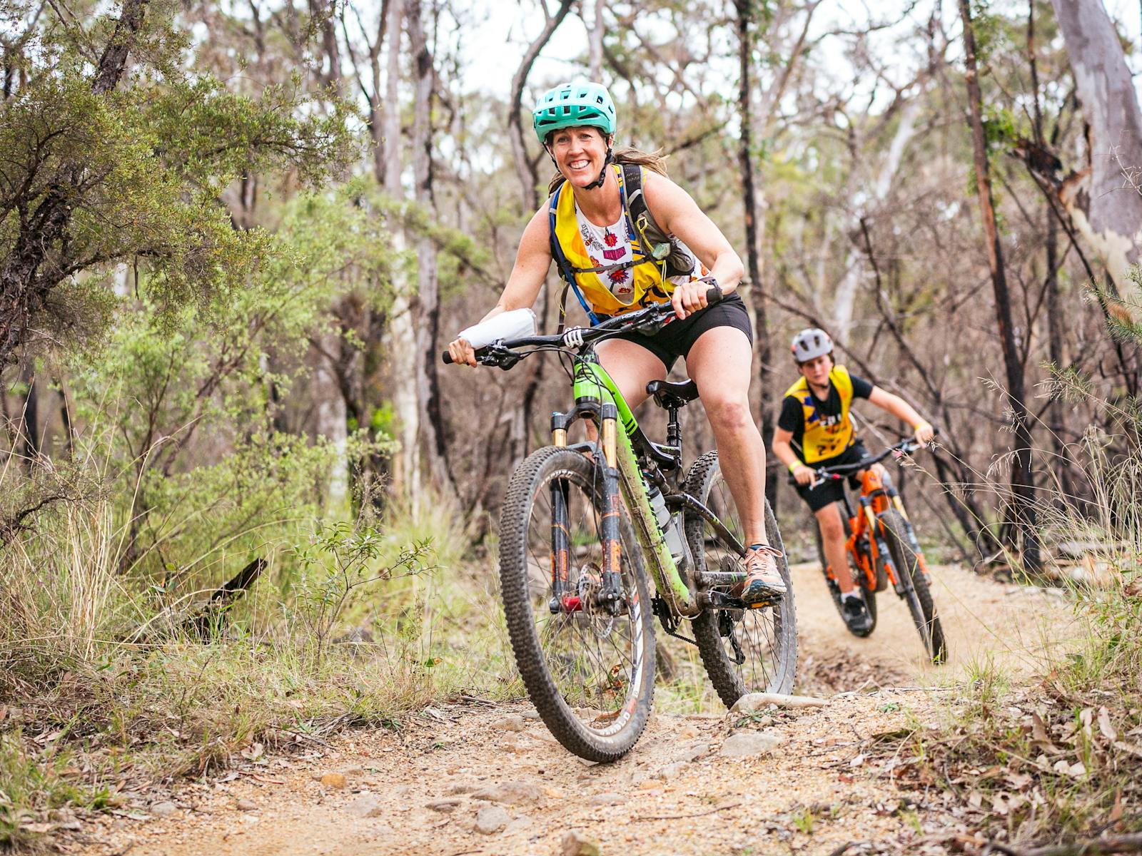 Two teammates ride down singletrack towards the camera
