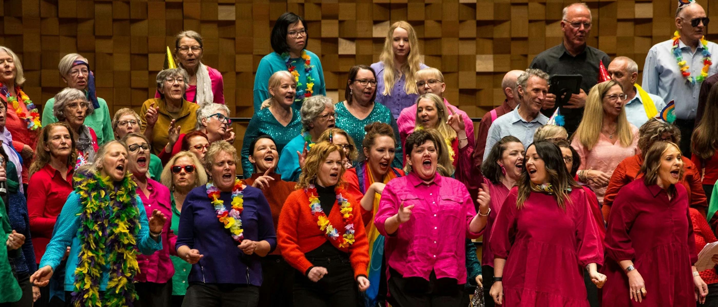 A group of people wearing colourful, festive clothing singing joyously together.