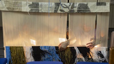 The back of a tapestry being woven by people on the other side