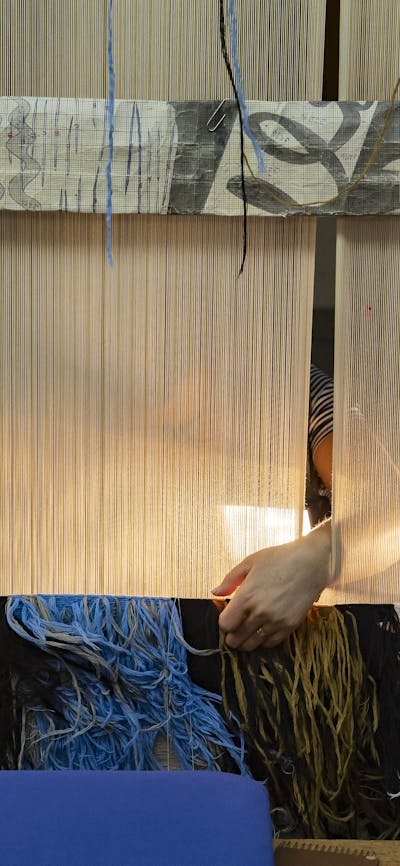The back of a tapestry being woven by people on the other side