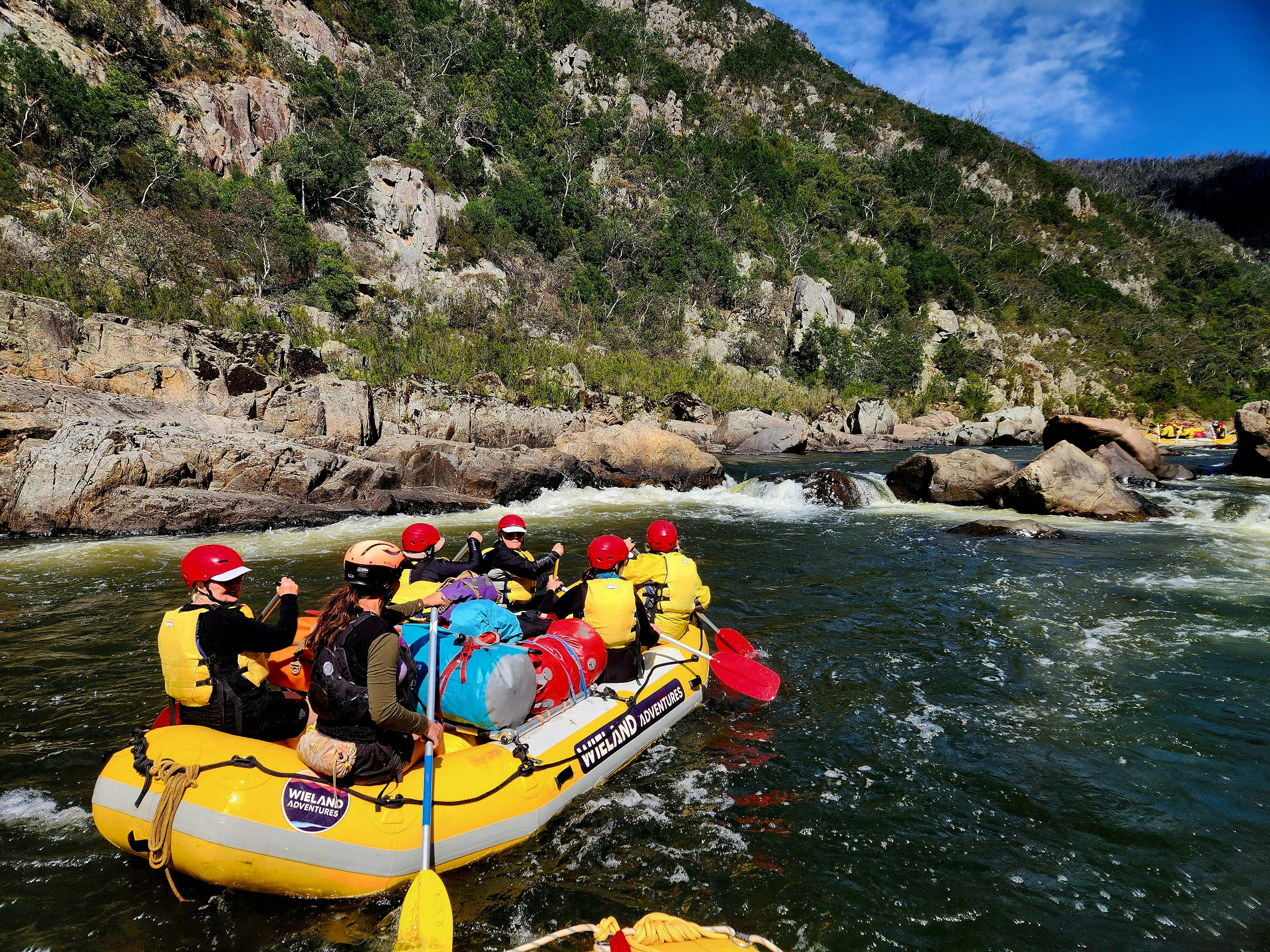 A group of clients with a guide in a yellow whitewater raft on the Snowy River on a sunny day.