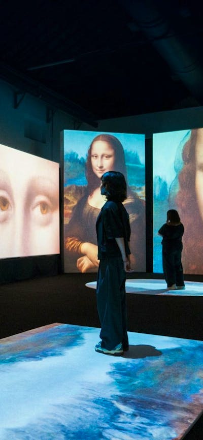 Visitors move through a digital gallery surrounded by immersive Mona Lisa projections.