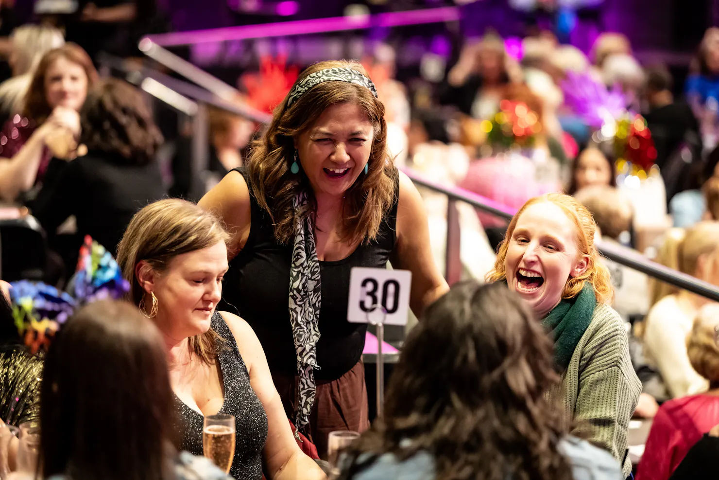 One lady standing between two ladies sitting at table 30, laughing