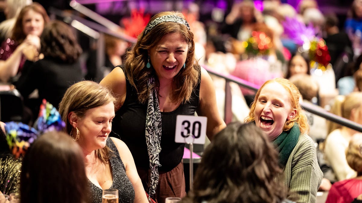 One lady standing between two ladies sitting at table 30, laughing