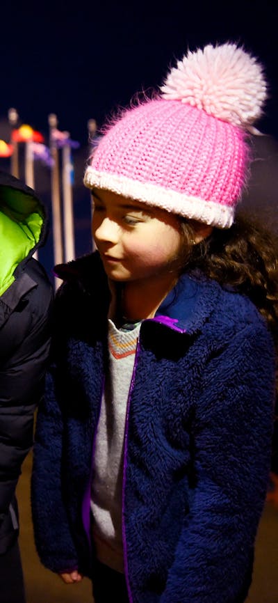 Two children stand outdoors at night using a telescope.