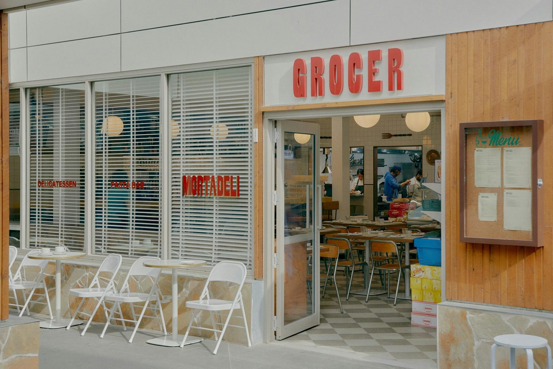 exterior shot of the entrance with a red sign and white tables and chairs outside