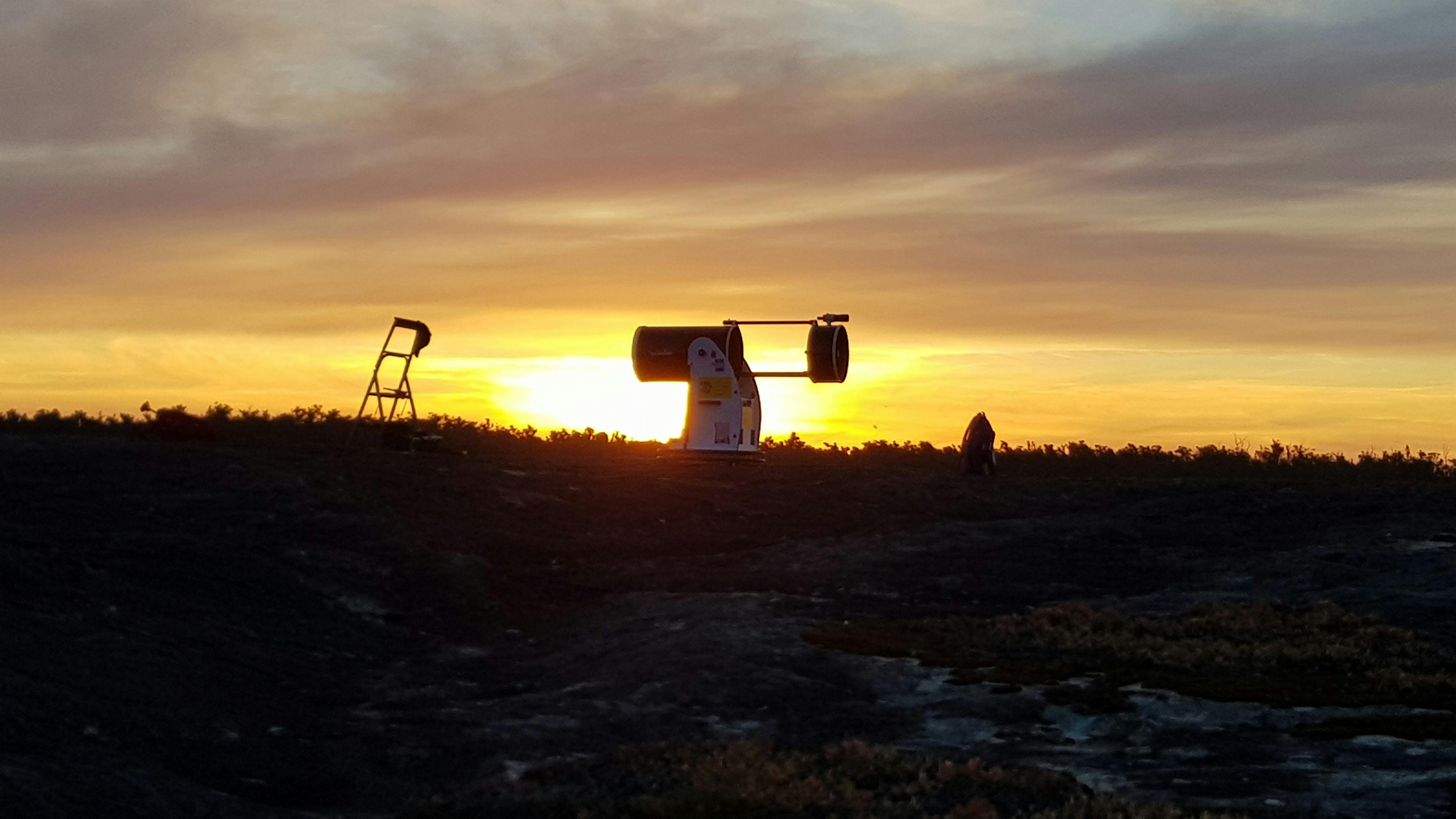 Very large professional telescope silhouette as sun sets in background. Warm yellow sky