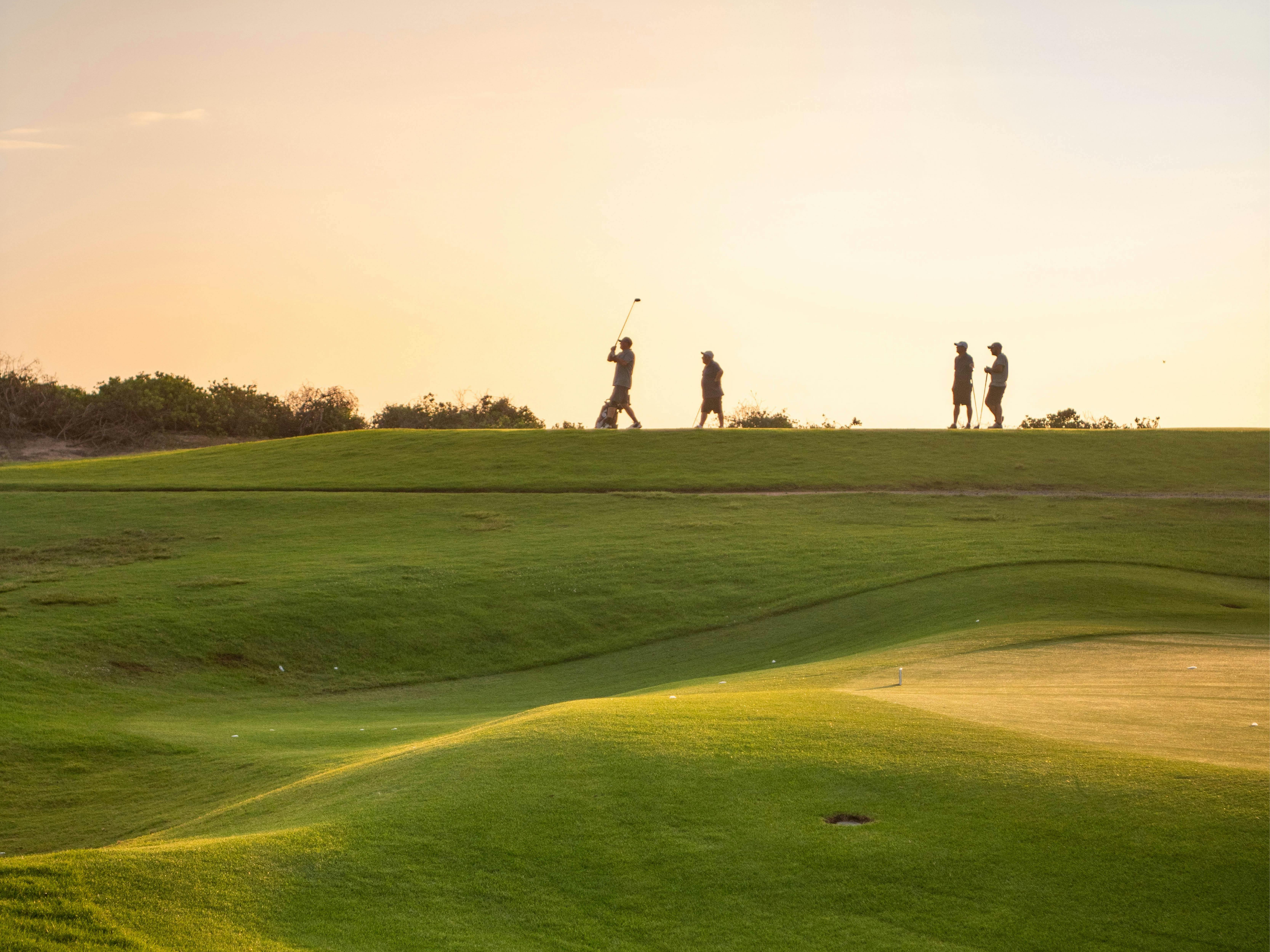 석양에 실루엣으로 드러난 골프 코스 위의 선수들