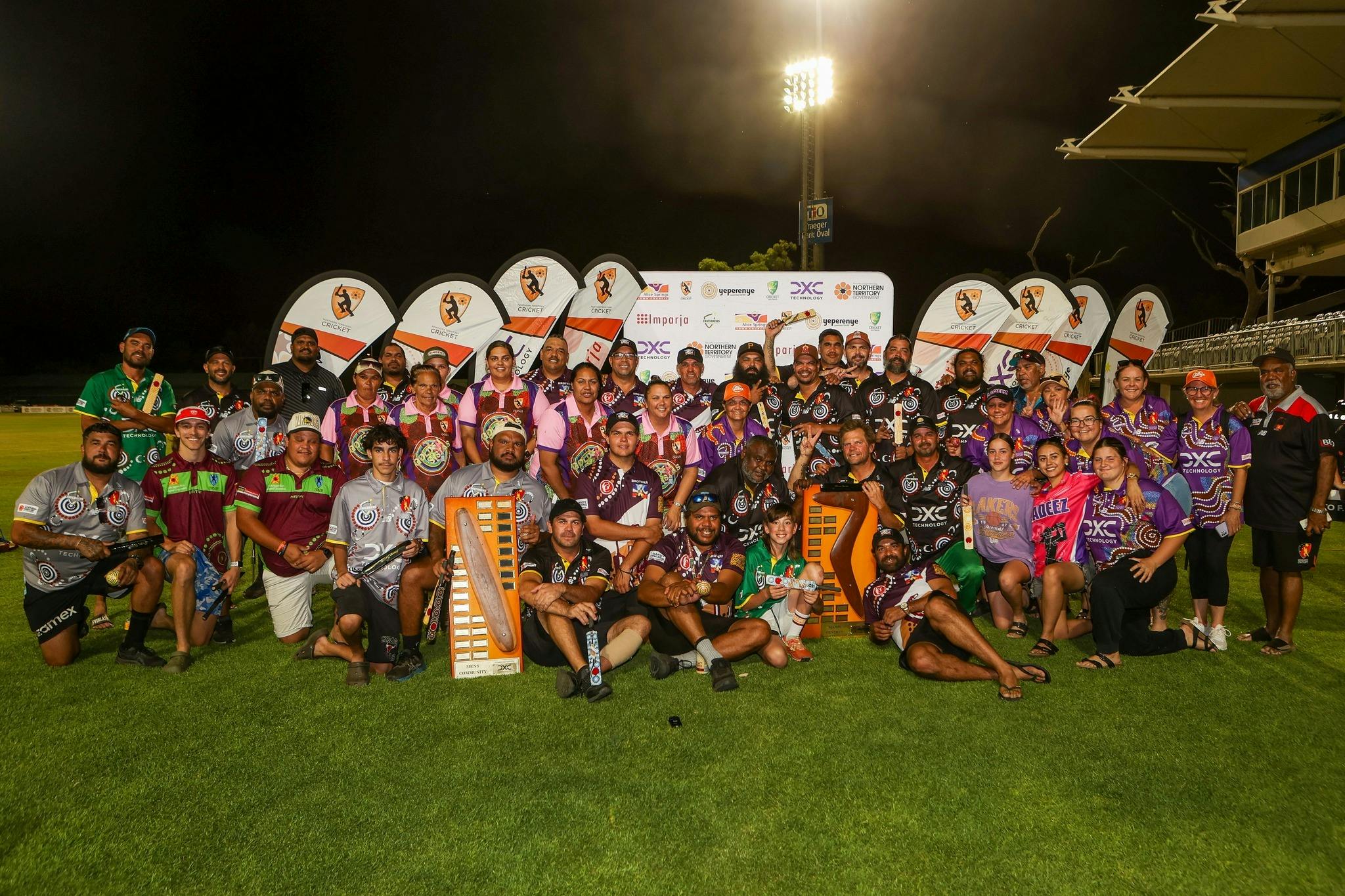 Group photo of participants from the Imparja Cup at night on the Traegar Park outfield