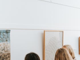 Three women looking at various artworks on a white wall