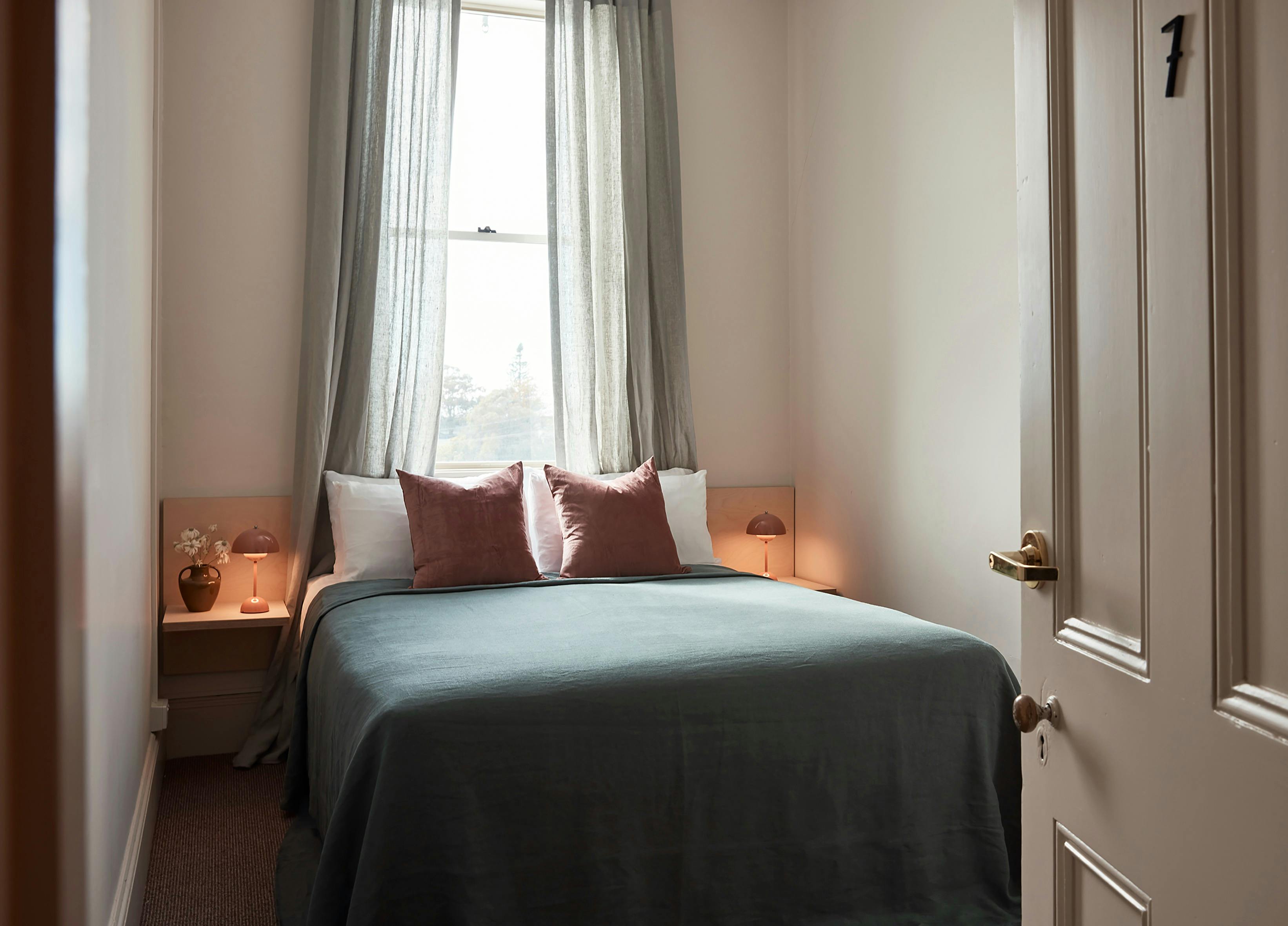 Cozy bedroom with soft grey curtains, green bedspread, and pink accent pillows
