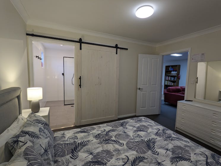 Entry to ensuite beside queen bed. Dressing table with mirror &  door to bedroom at foot of bed.