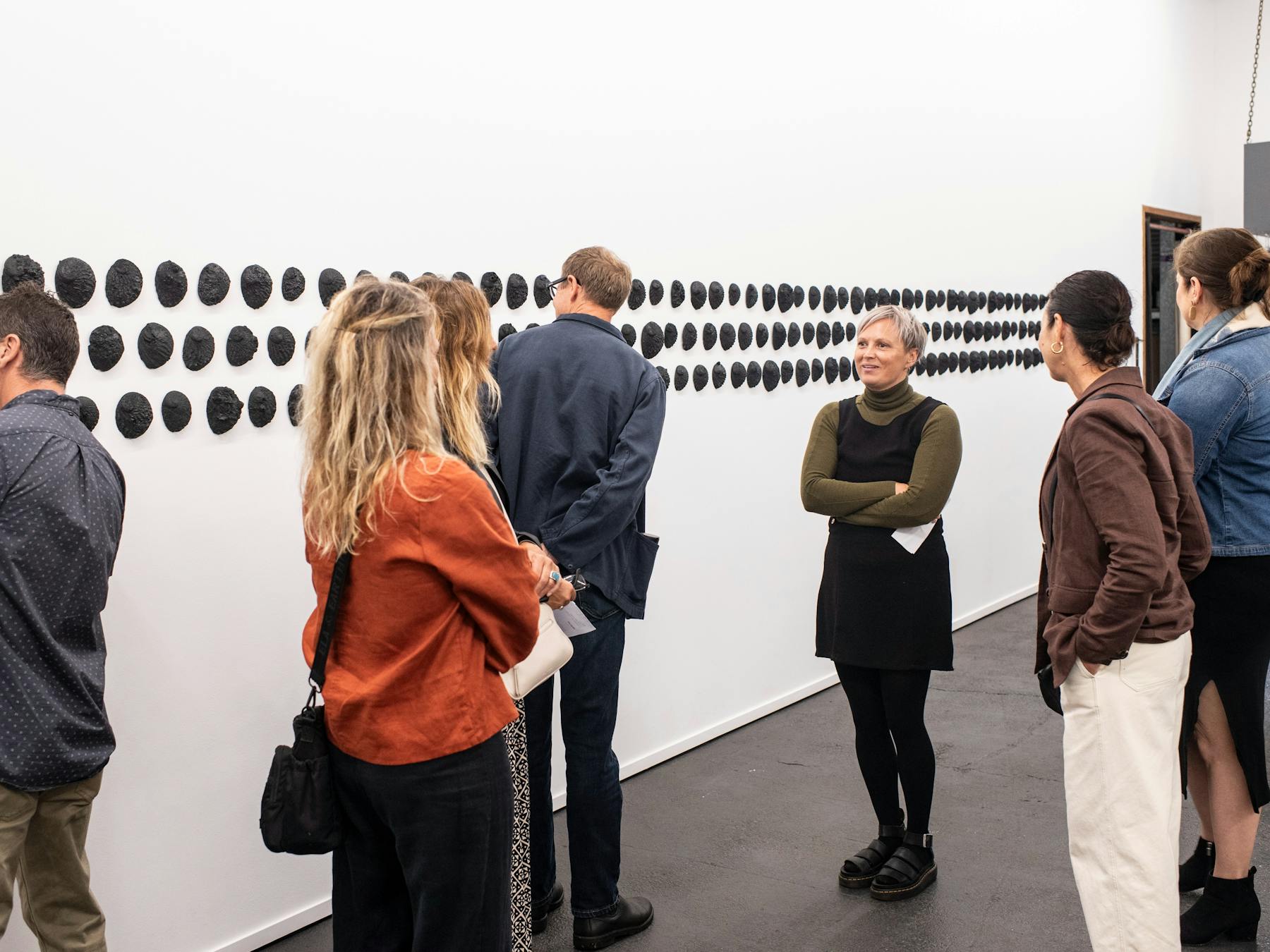 A group of people looking at the wounds exhibition showcasing black shells on the walls