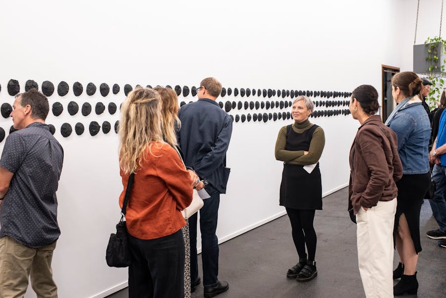 A group of people looking at the wounds exhibition showcasing black shells on the walls