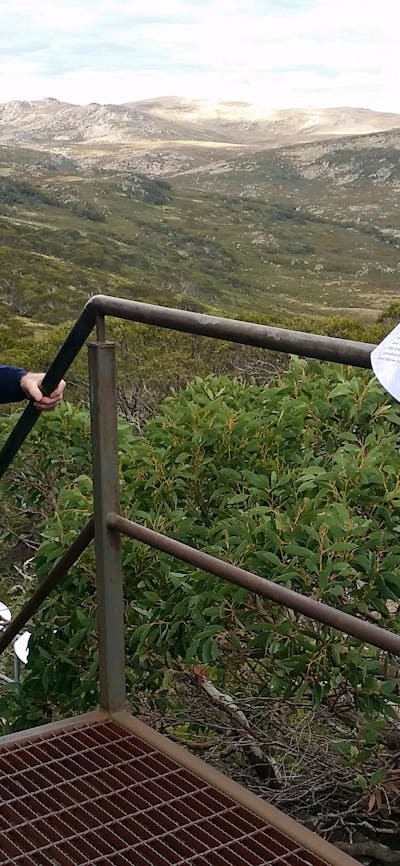 man walking up metal stairs with valley and mountains behind