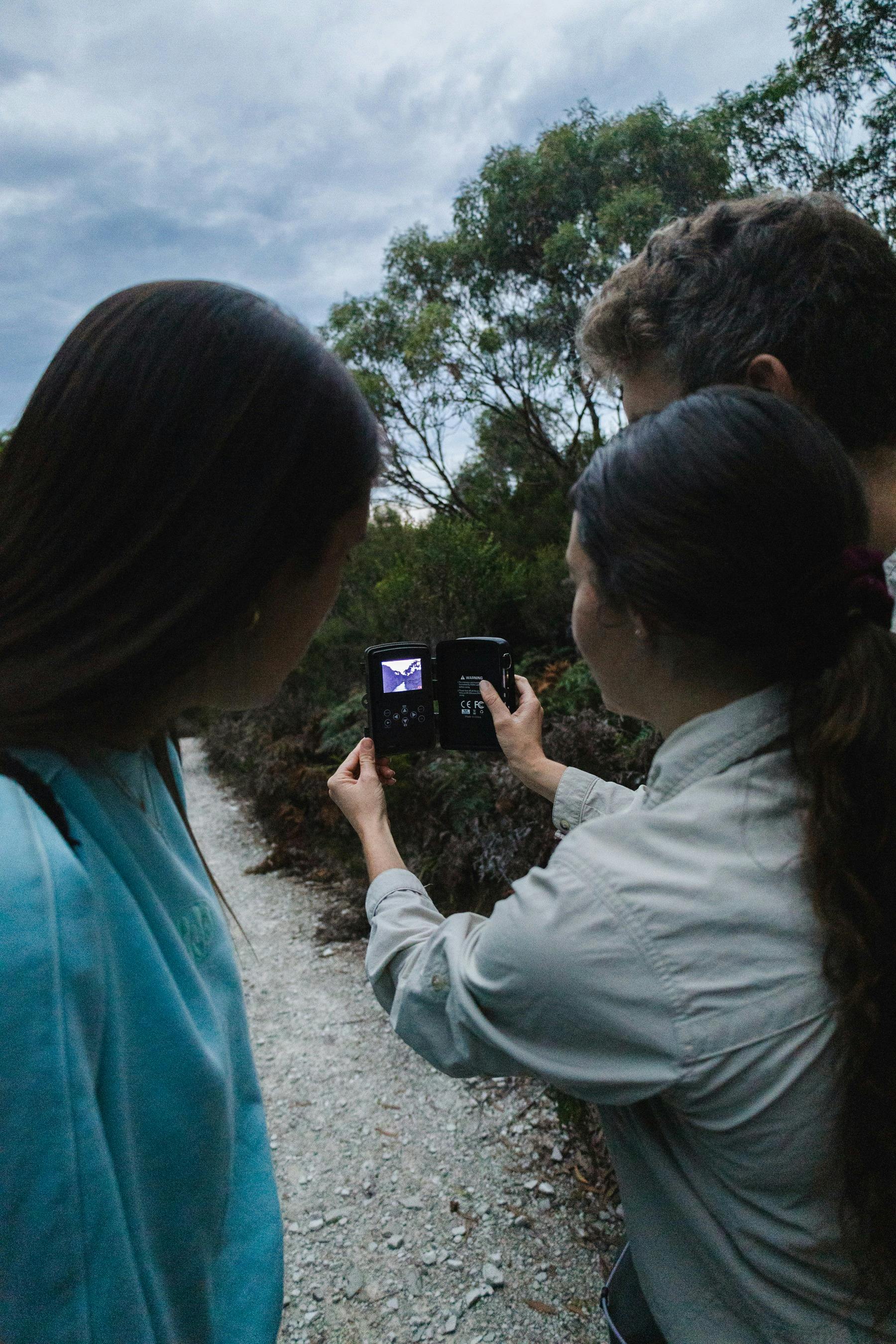 Guide holding up a wildlife detection camera, showing a guest how it works.