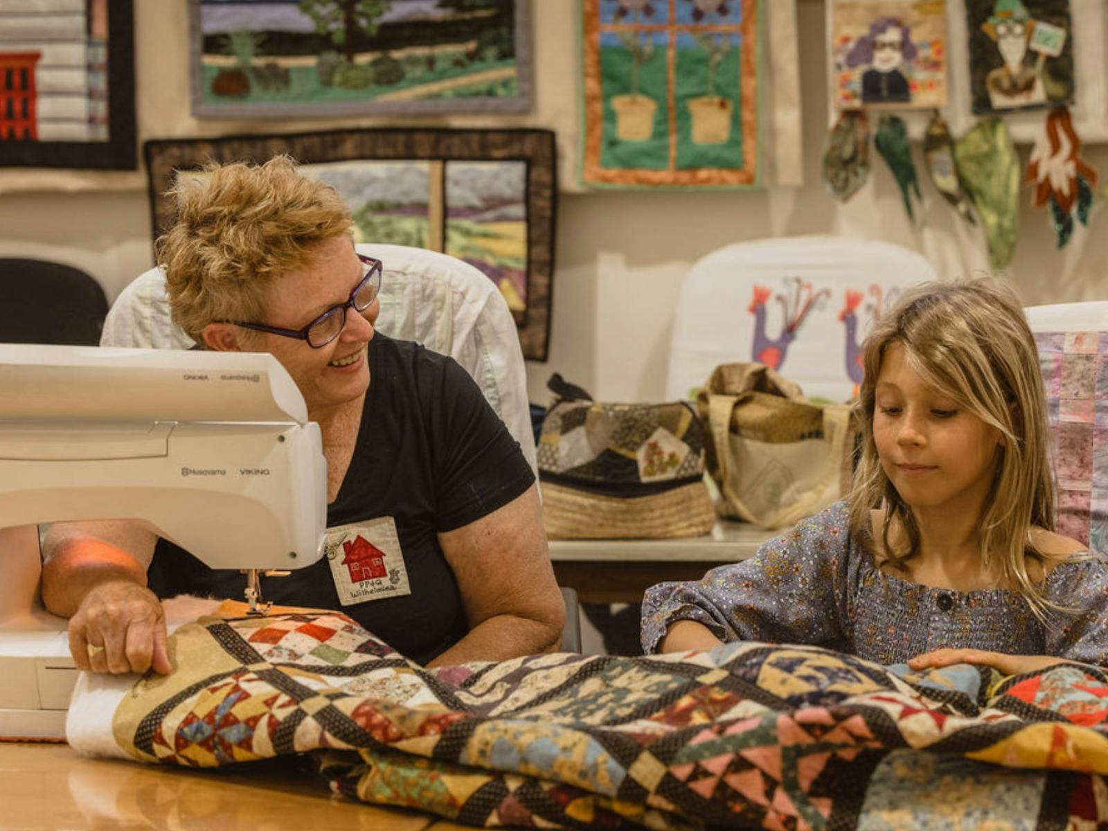 A member of the Pinjarra Patchwork and Quilters club demonstrates quilt making to a child