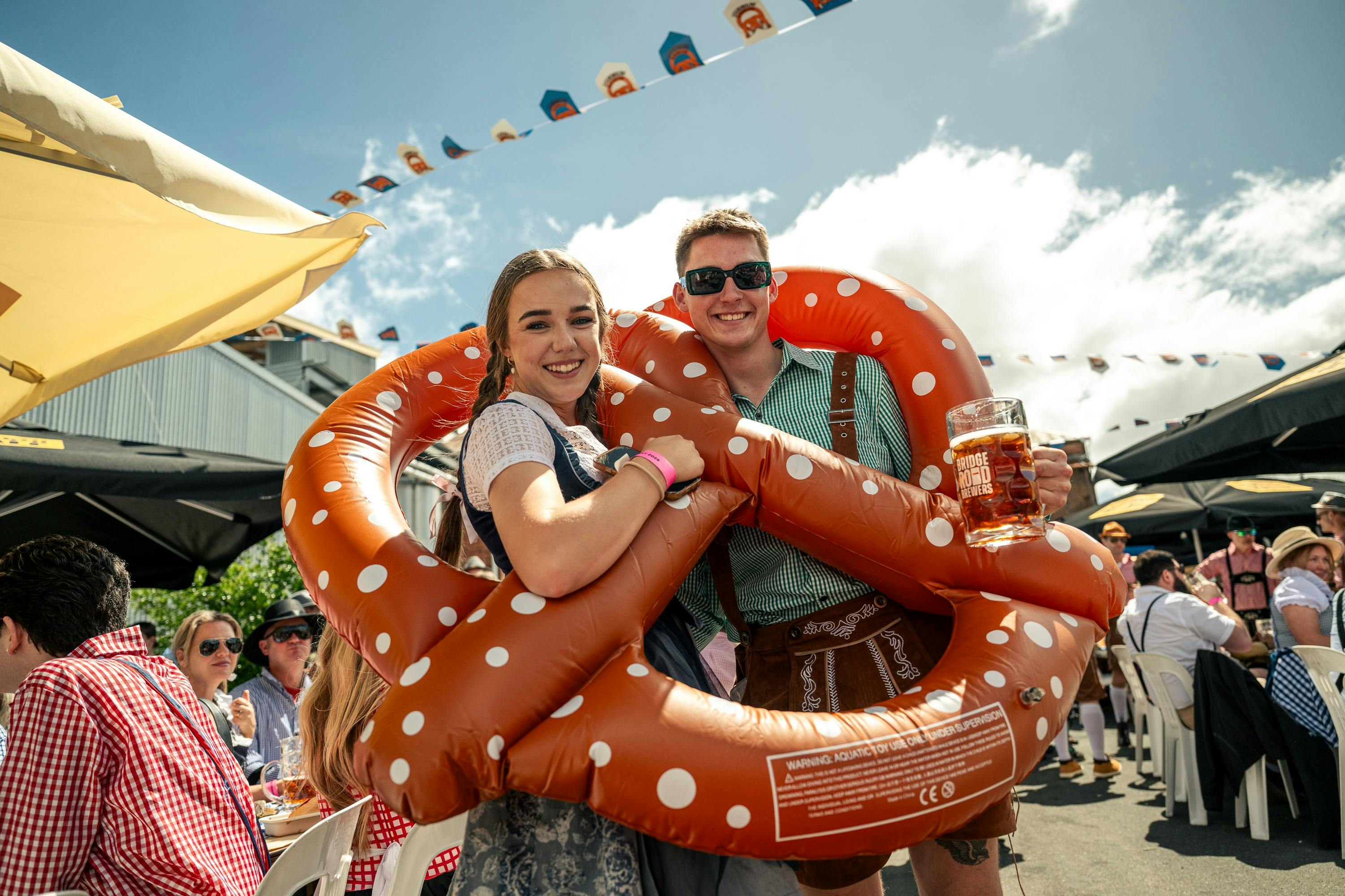 Couple standing inside an inflatable pretzel holding beers.