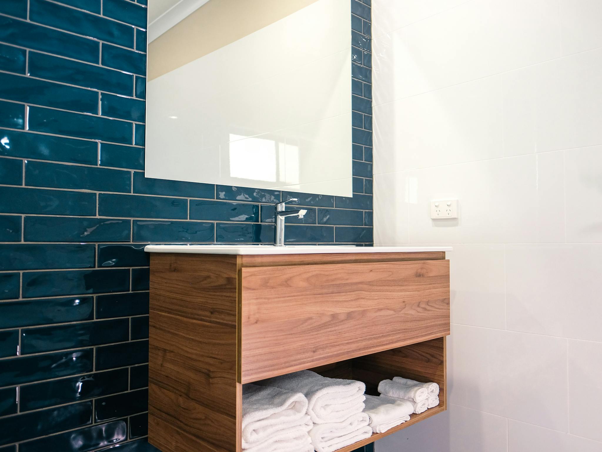 Wooden vanity on a navy blue subway tile wall and large mirror