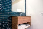 Wooden vanity on a navy blue subway tile wall and large mirror